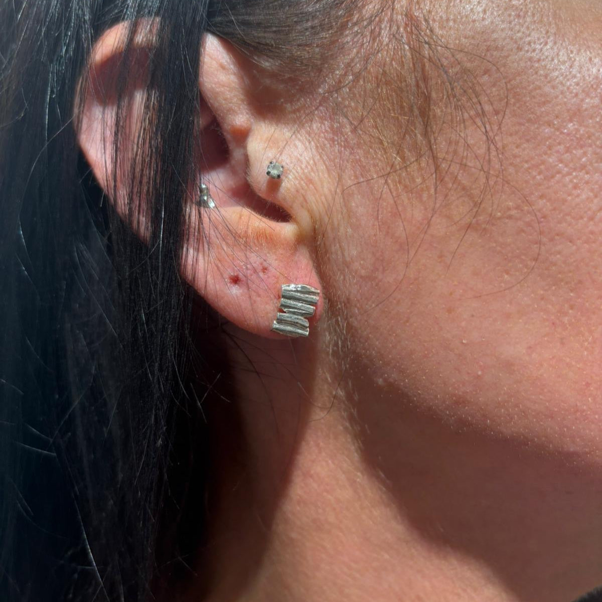 Close-up of an ear with multiple earrings against a blurred background
