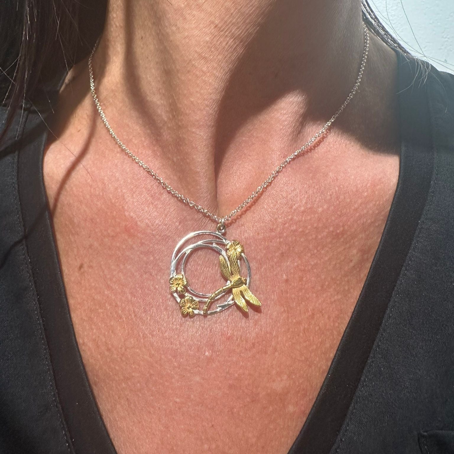 Close-up of a necklace with a circular pendant on a person wearing a black top.