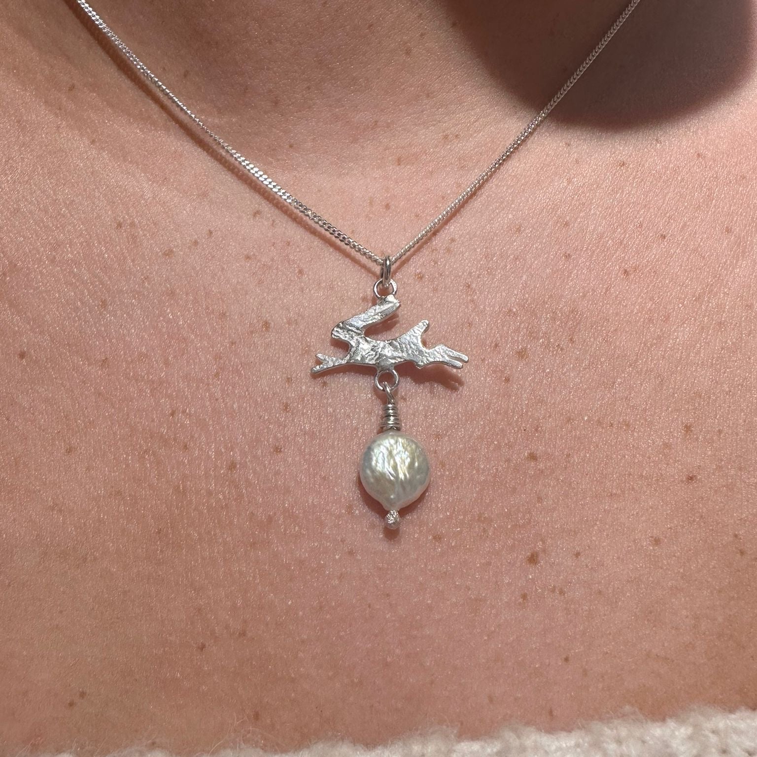 Necklace with a silver pendant and pearl drop worn by a person.