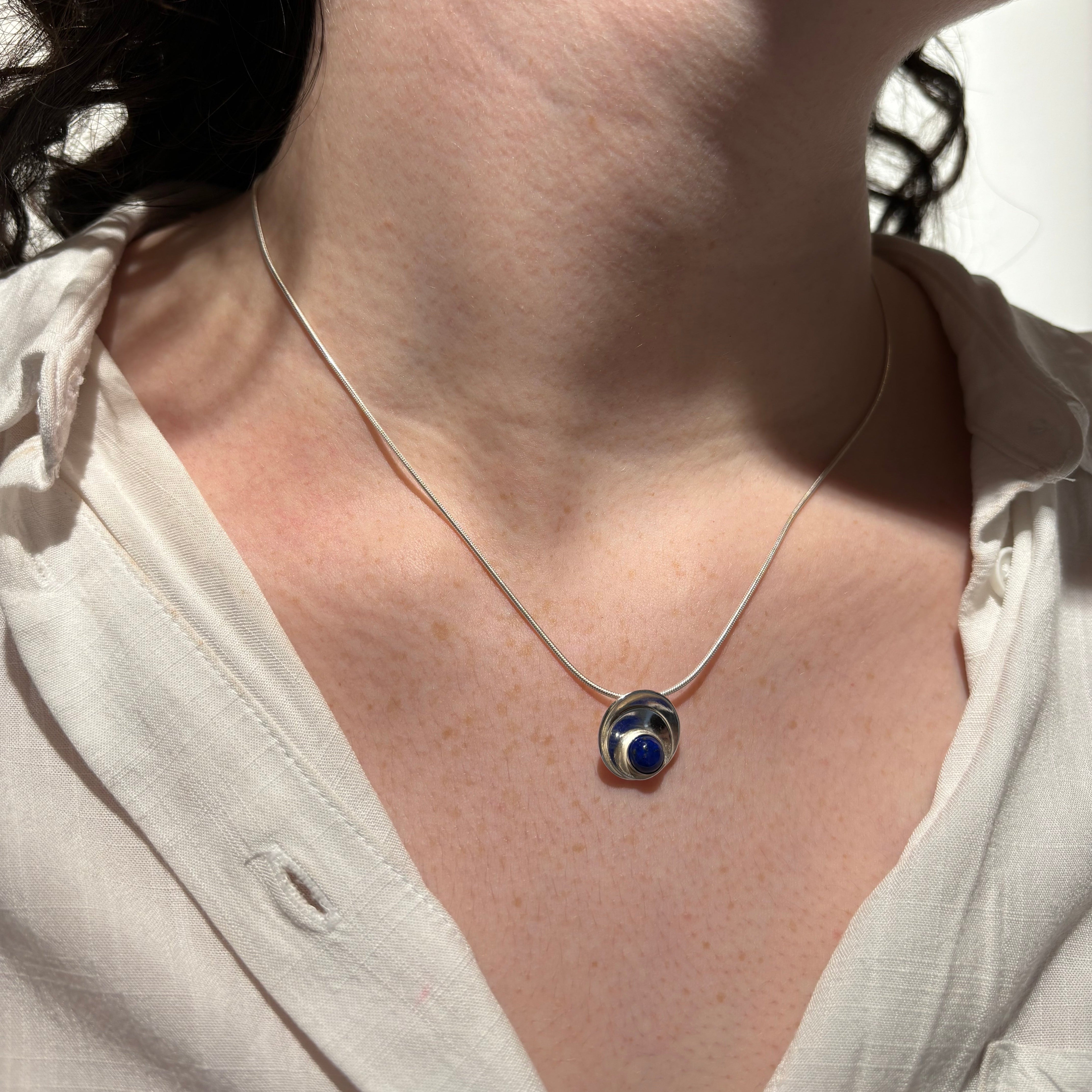 Person wearing a necklace with a pendant on a light background