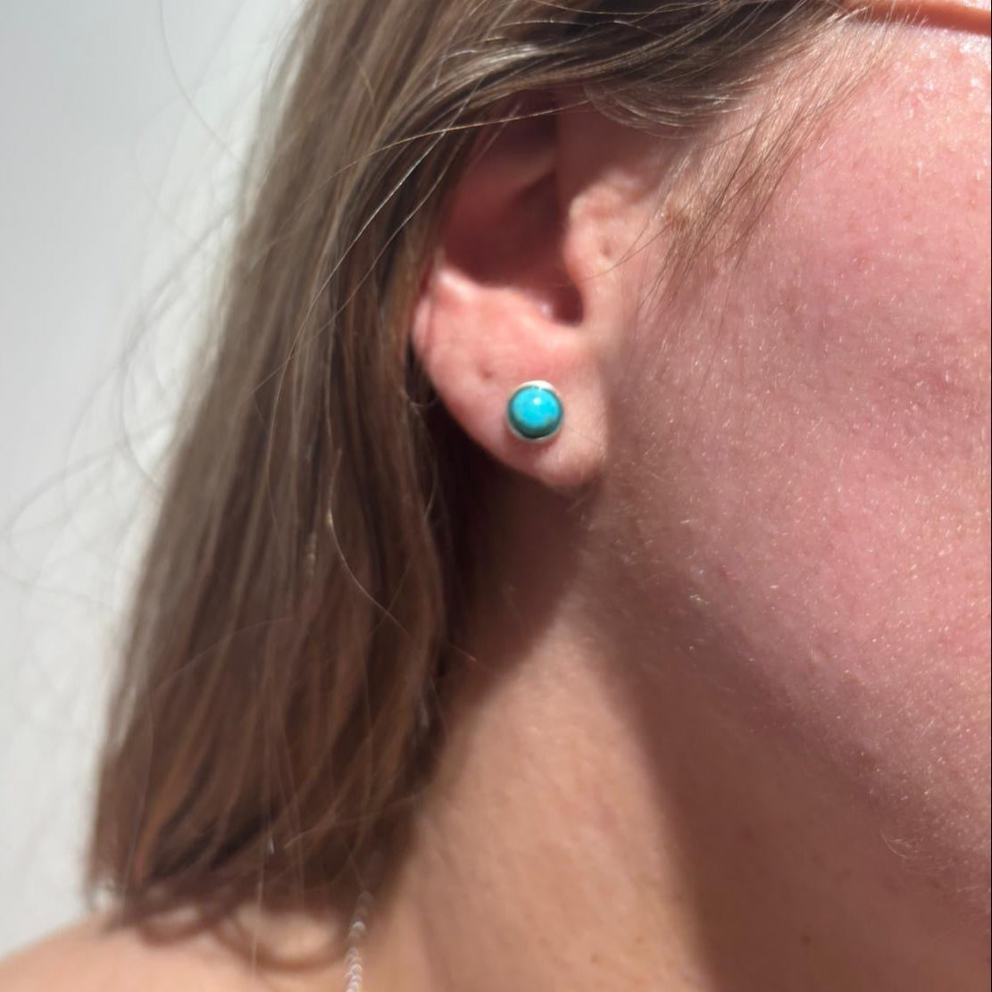 Close-up of an ear wearing a turquoise earring against a white background