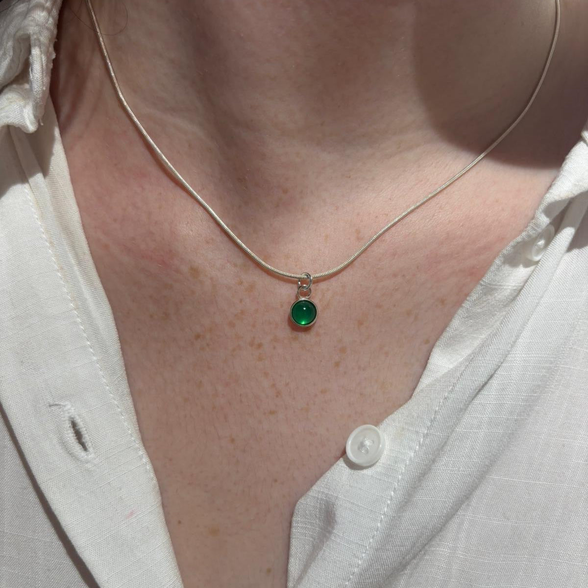 Necklace with a green pendant worn by a person in a white shirt.
