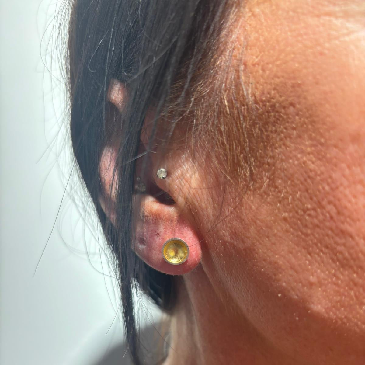 Close-up of a person wearing a gold earring with a plain background
