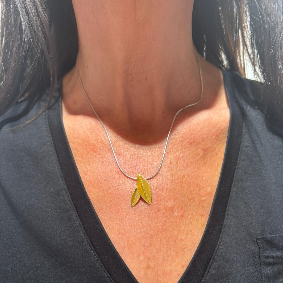 Person wearing a necklace with a yellow pendant against a black background