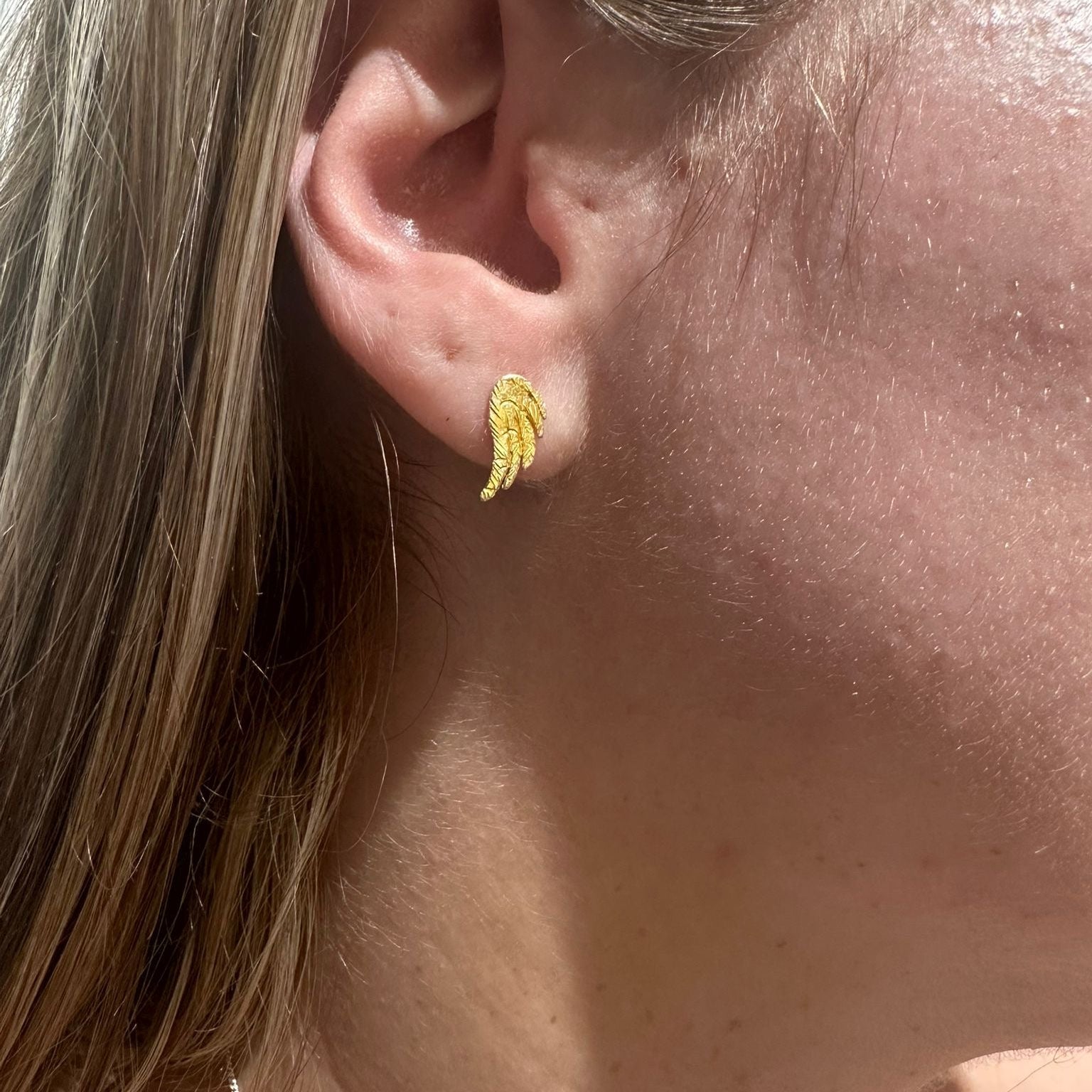 Close-up of a person wearing a gold Wing Stud earring